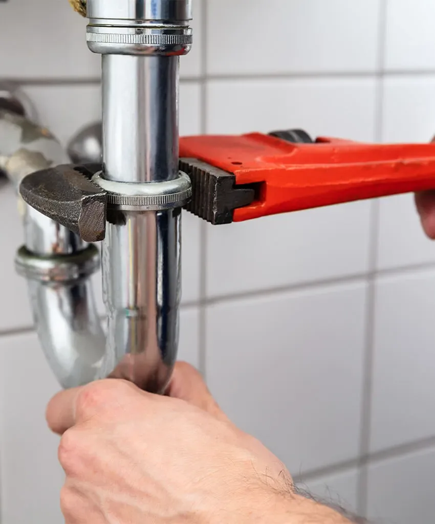 Plumber tightening a drain pipe beneath a sink